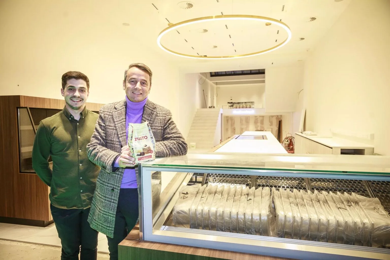 Two men holding Zùsto in a newly opened Belgian patisserie