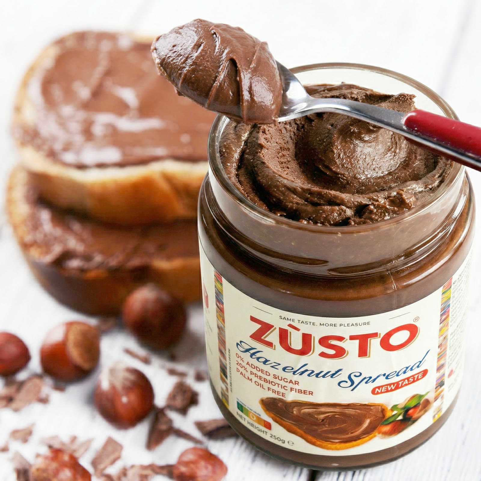 A spoon lifting Zùsto hazelnut spread above an open jar, beside thickly spread bread